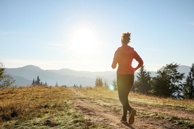 Photo of Sporty woman running in mountains, back view