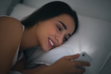 Photo of Young woman with nomophobia using smartphone in bed at night. Insomnia concept