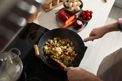 Photo of Man stirring mix of fresh vegetables in frying pan, above view