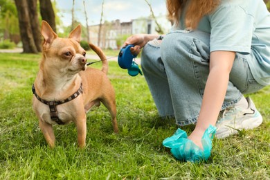 Photo of Woman picking up her dog's poop from green grass in park, closeup