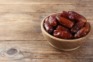 Photo of Sweet dried dates in bowl on wooden table. Space for text