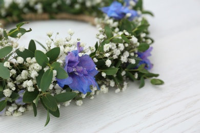 Beautiful flower wreath on white wooden background, closeup