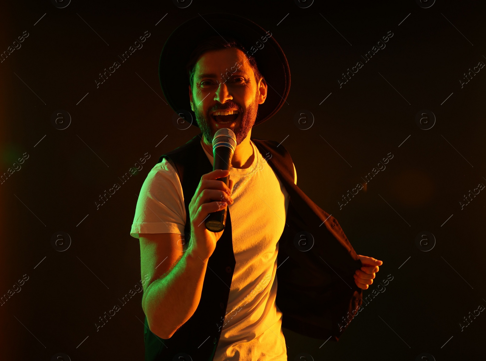 Photo of Handsome man with microphone singing in neon lights on dark background