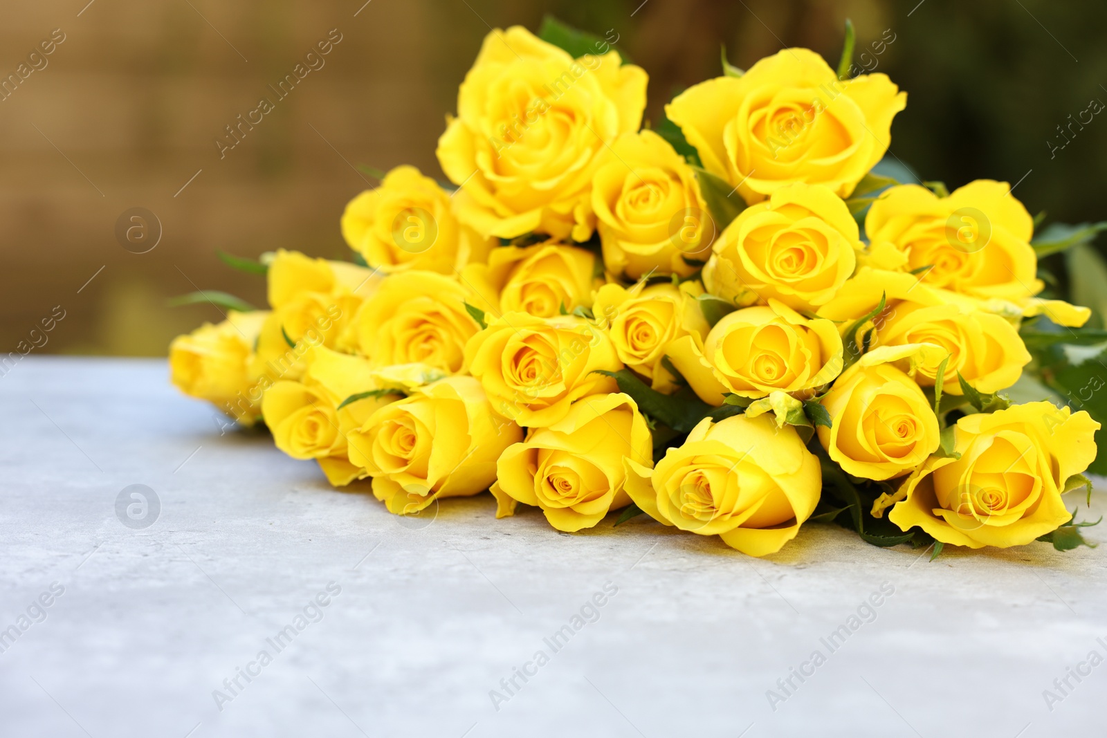 Photo of Beautiful bouquet of yellow roses on light table outdoors