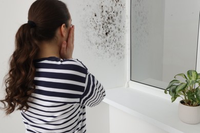Image of Shocked woman looking at affected with mold window slope in room
