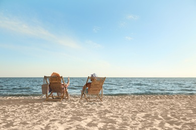 Photo of Young couple relaxing in deck chairs on beach near sea