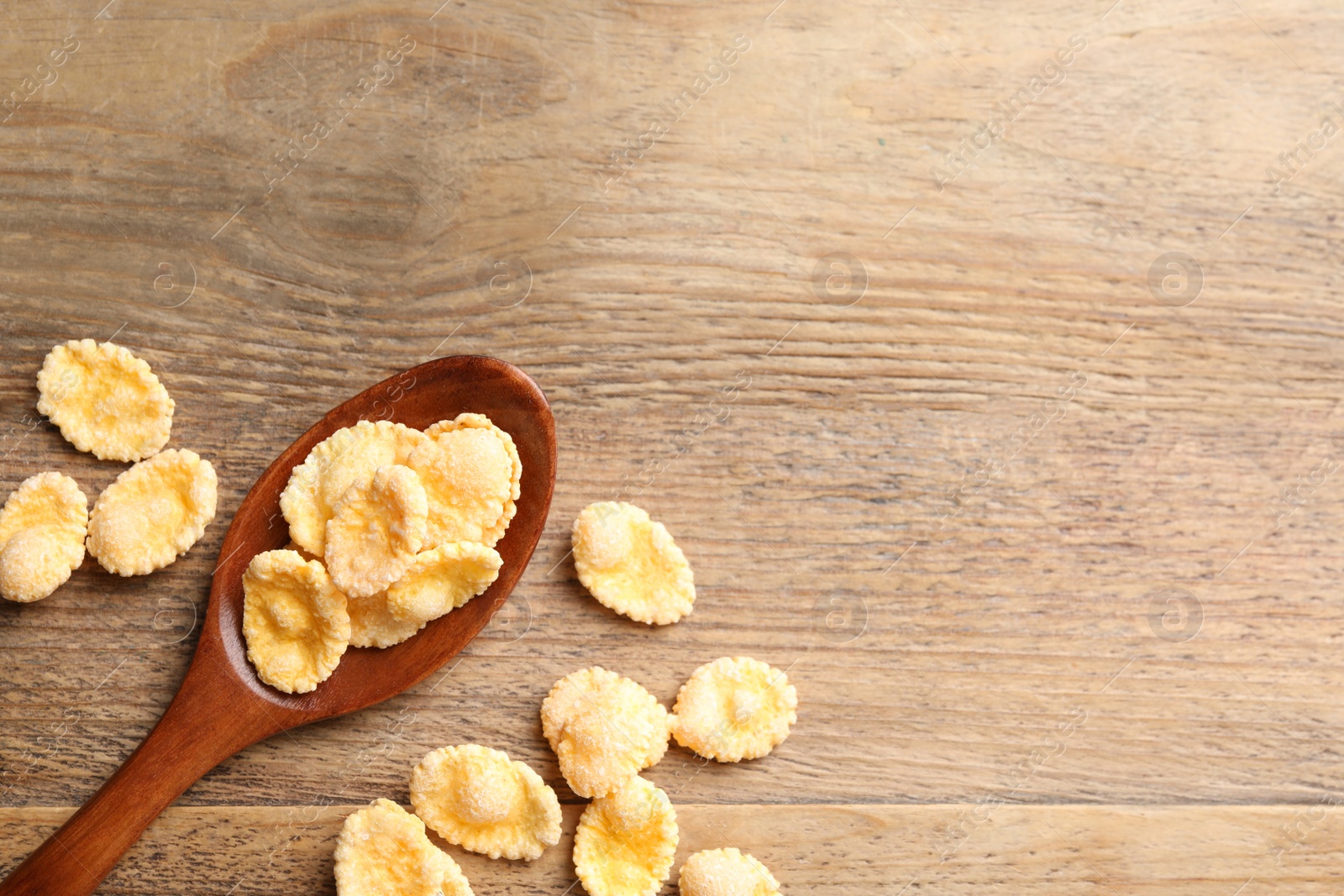 Photo of Spoon and tasty corn flakes on wooden table, flat lay. Space for text