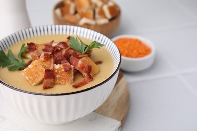 Photo of Delicious lentil soup with bacon and parsley in bowl on white tiled table, closeup