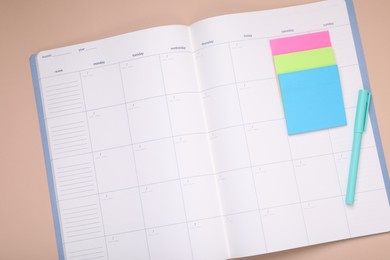 Photo of Open monthly planner, blank sticky notes and pen on beige background, top view. Space for text
