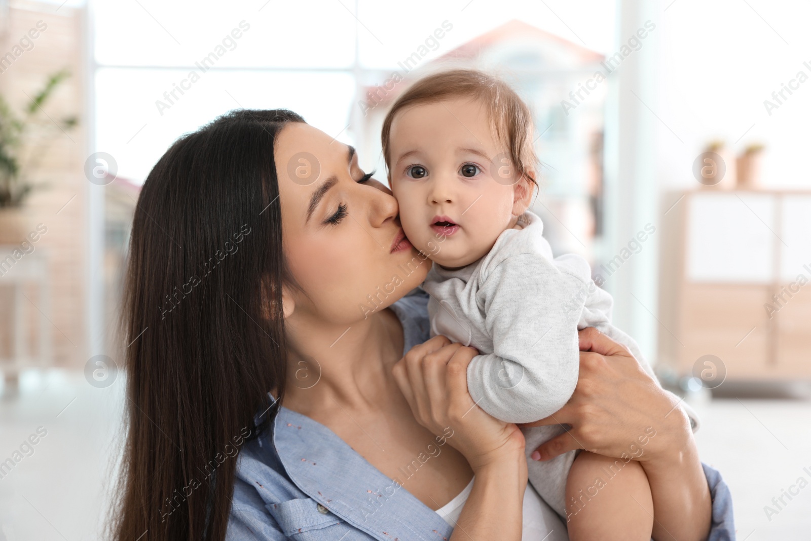 Photo of Happy young mother kissing her adorable baby in living room