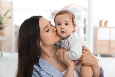 Happy young mother kissing her adorable baby in living room