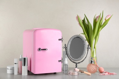 Photo of Cosmetic refrigerator and skin care products on beige background