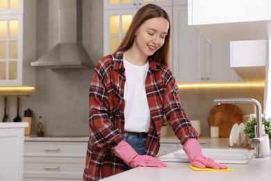 Photo of Woman cleaning white marble table with microfiber cloth in kitchen