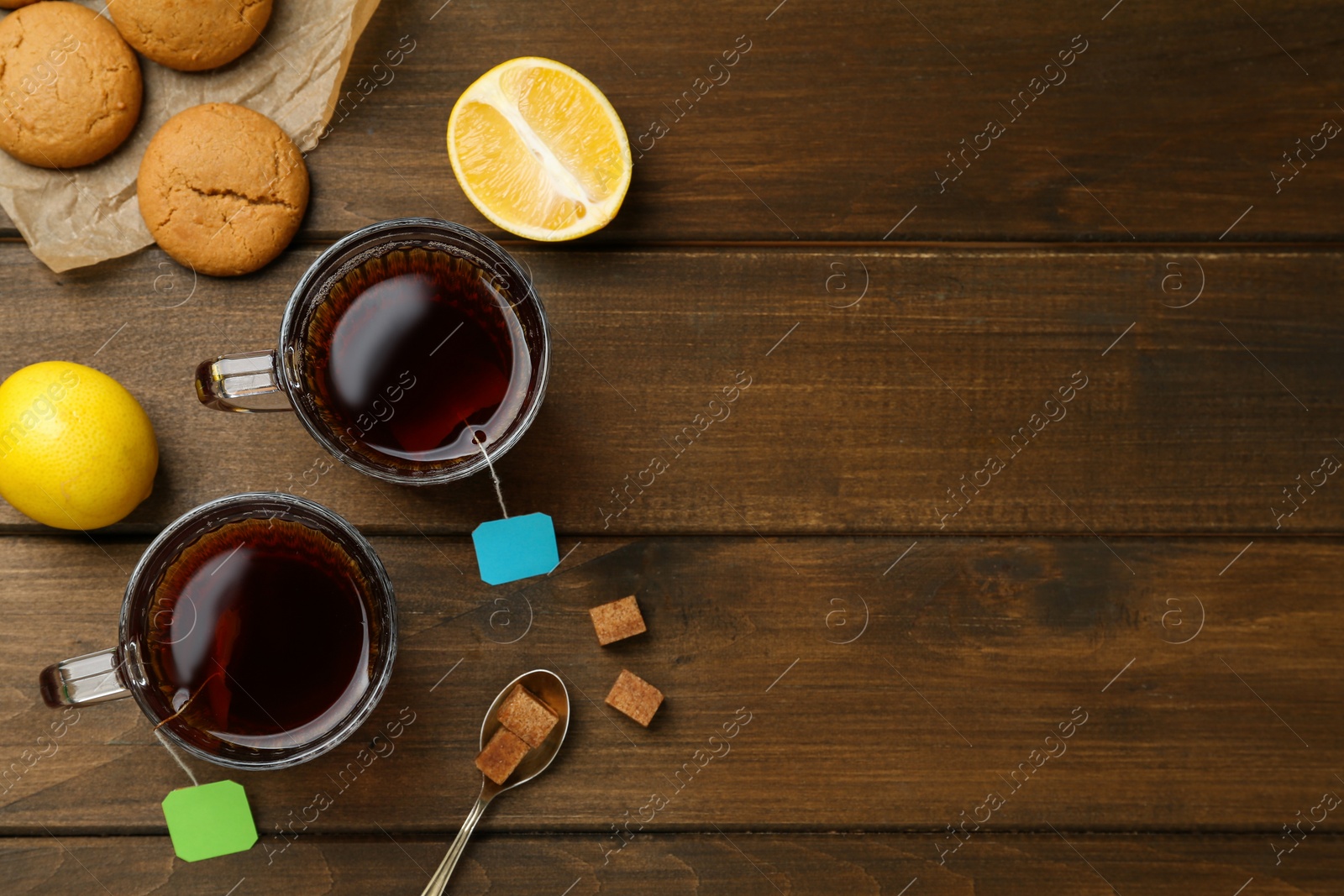 Photo of Tea bags in glass cups of hot water, cookies and sugar cubes on wooden table, flat lay. Space for text