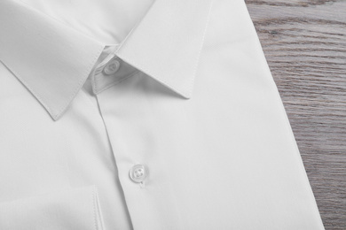 Photo of Stylish white shirt on wooden table, closeup. Dry-cleaning service