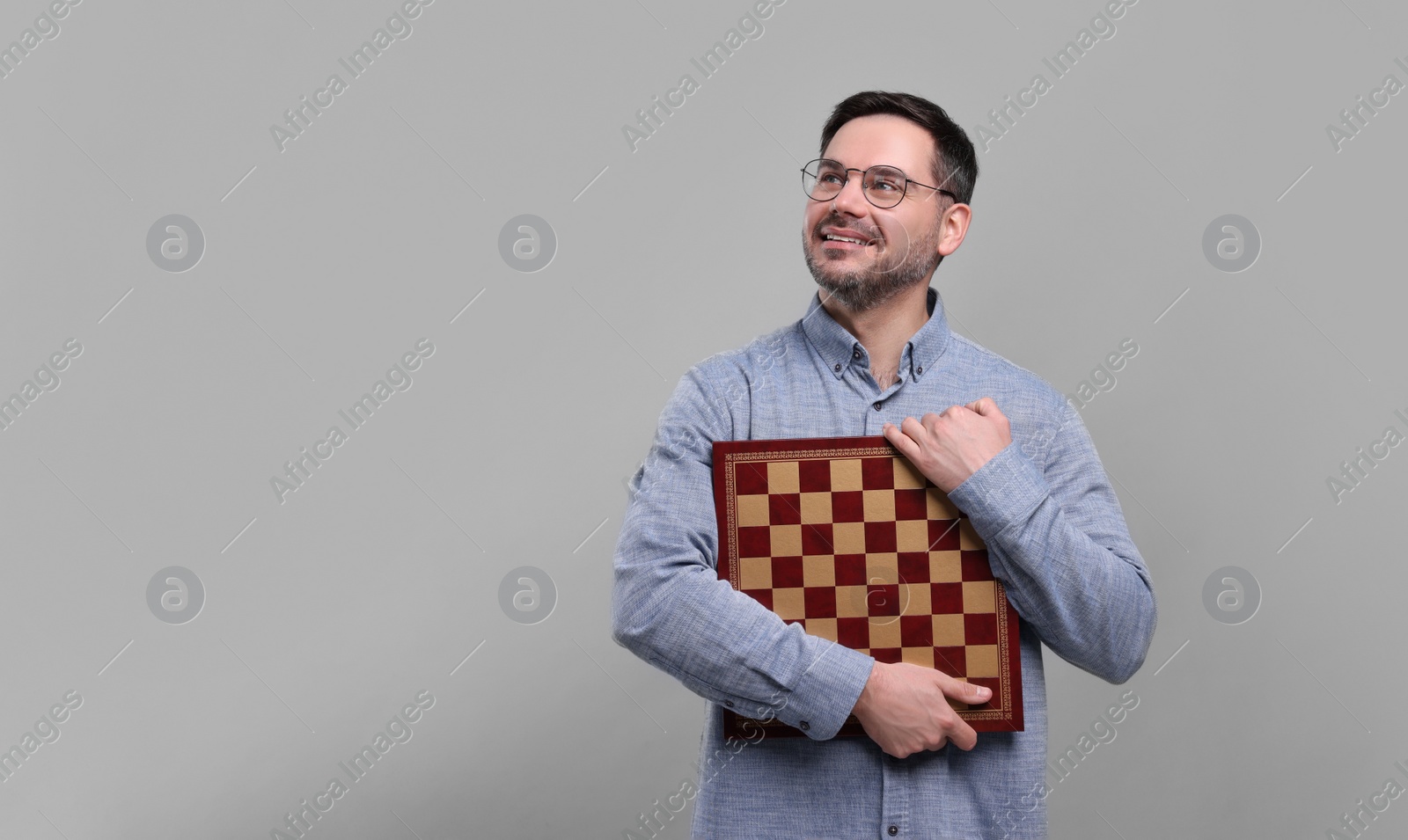 Photo of Smiling man holding chessboard on light grey background, space for text