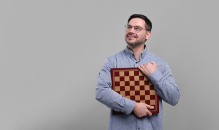 Photo of Smiling man holding chessboard on light grey background, space for text