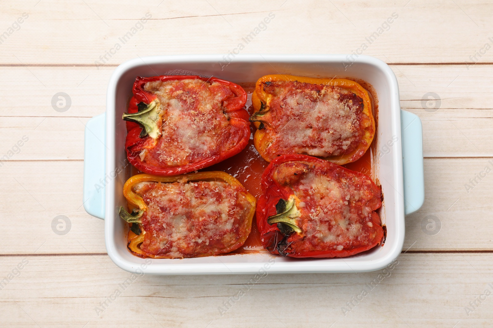 Photo of Tasty stuffed peppers in dish on light wooden table, top view