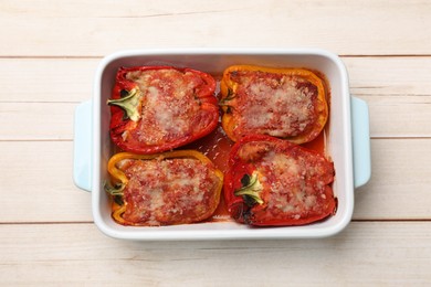 Photo of Tasty stuffed peppers in dish on light wooden table, top view