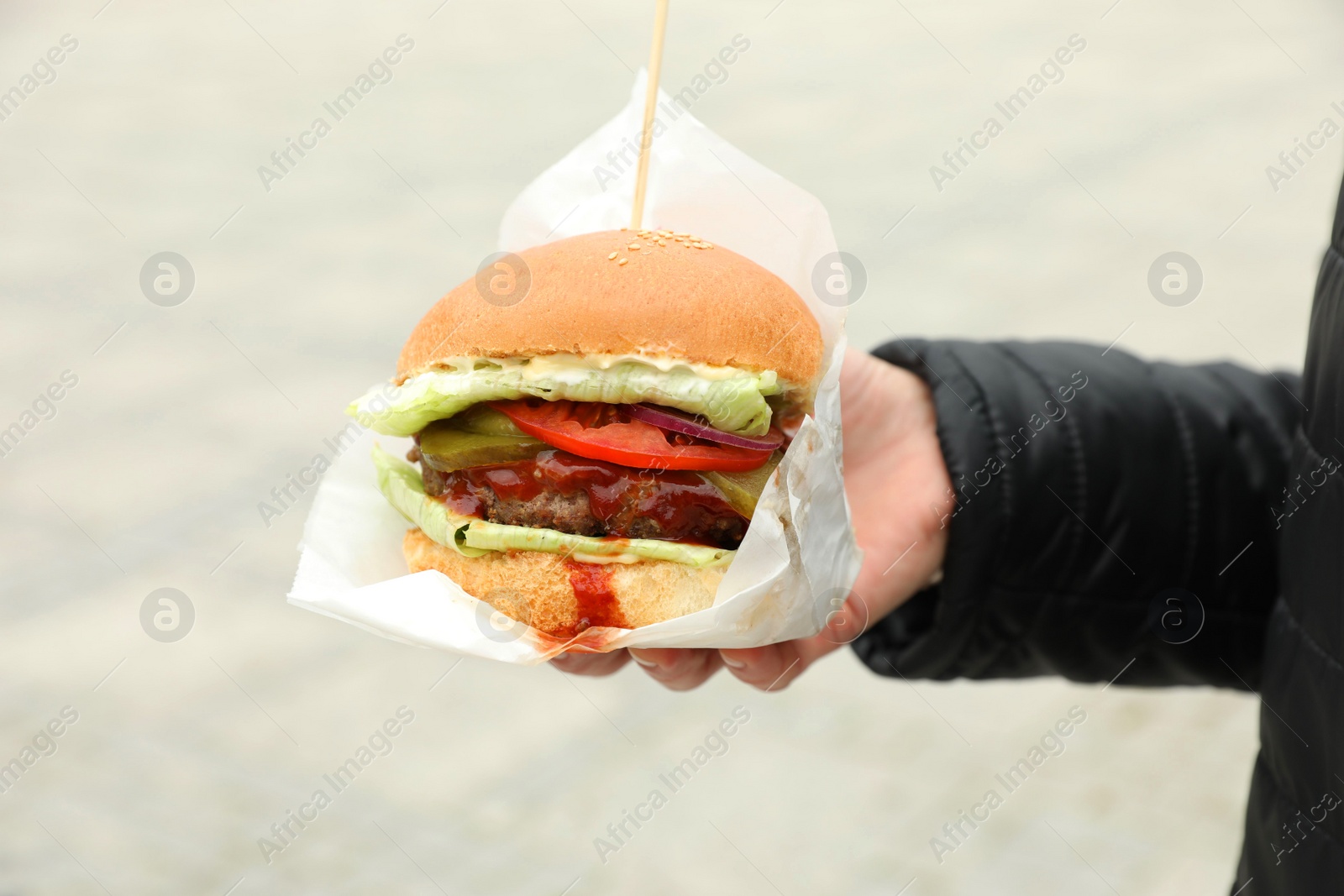 Photo of Woman holding fresh delicious burger outdoors, closeup. Street food