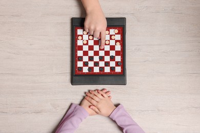 Children playing checkers at light wooden table, top view