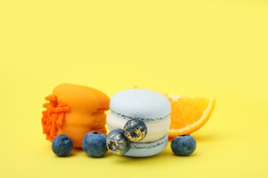 Photo of Delicious macarons, blueberries and orange slice on yellow background, closeup