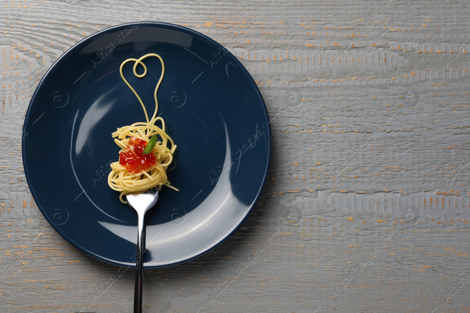 Photo of Heart made with spaghetti and fork on grey wooden table, top view. Space for text