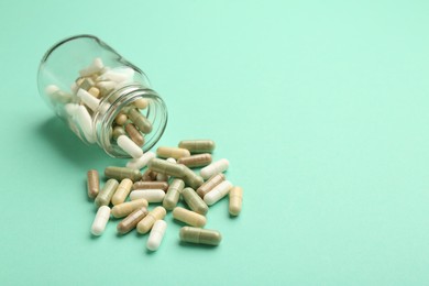 Photo of Vitamin pills and bottle on mint color background. Space for text