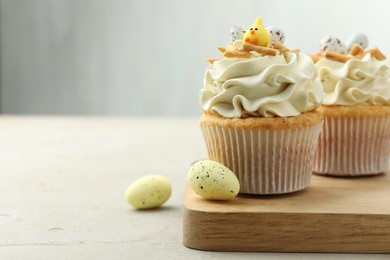 Photo of Tasty Easter cupcakes with vanilla cream and candies on gray table, space for text