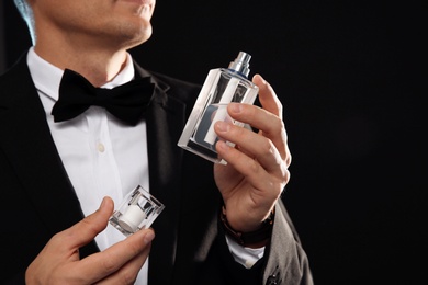 Photo of Young man with perfume bottle on black background, closeup