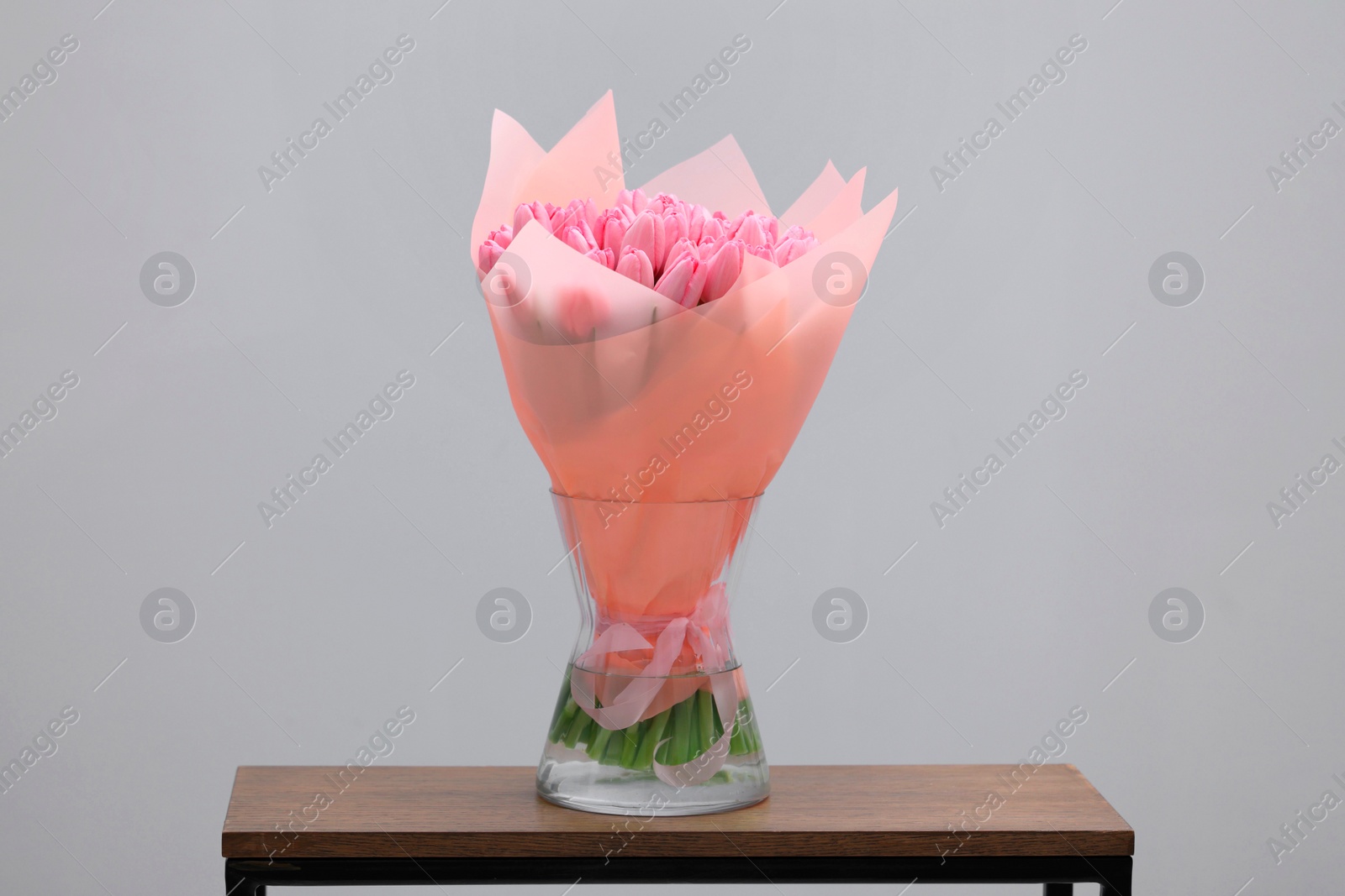 Photo of Bouquet of beautiful pink tulips in vase on wooden table against light grey background