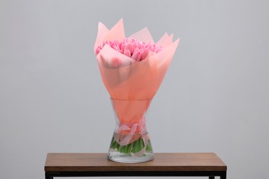 Bouquet of beautiful pink tulips in vase on wooden table against light grey background