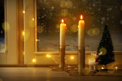 Image of Burning candles and festive decor on window sill indoors. Christmas eve