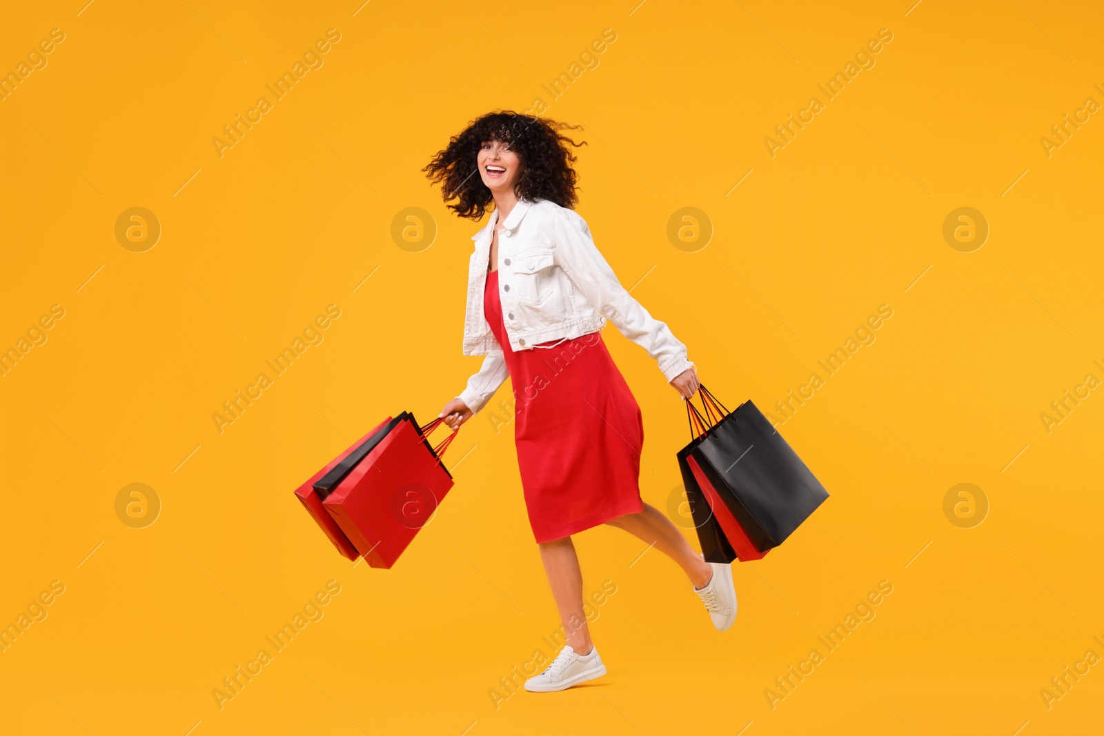 Photo of Happy young woman with shopping bags on yellow background