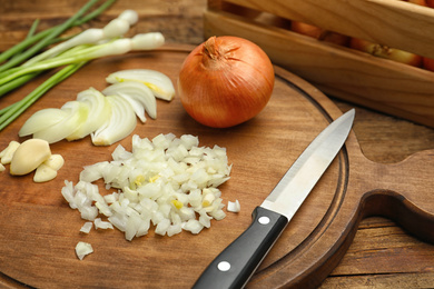 Photo of Board with cut onion and garlic on wooden table, closeup