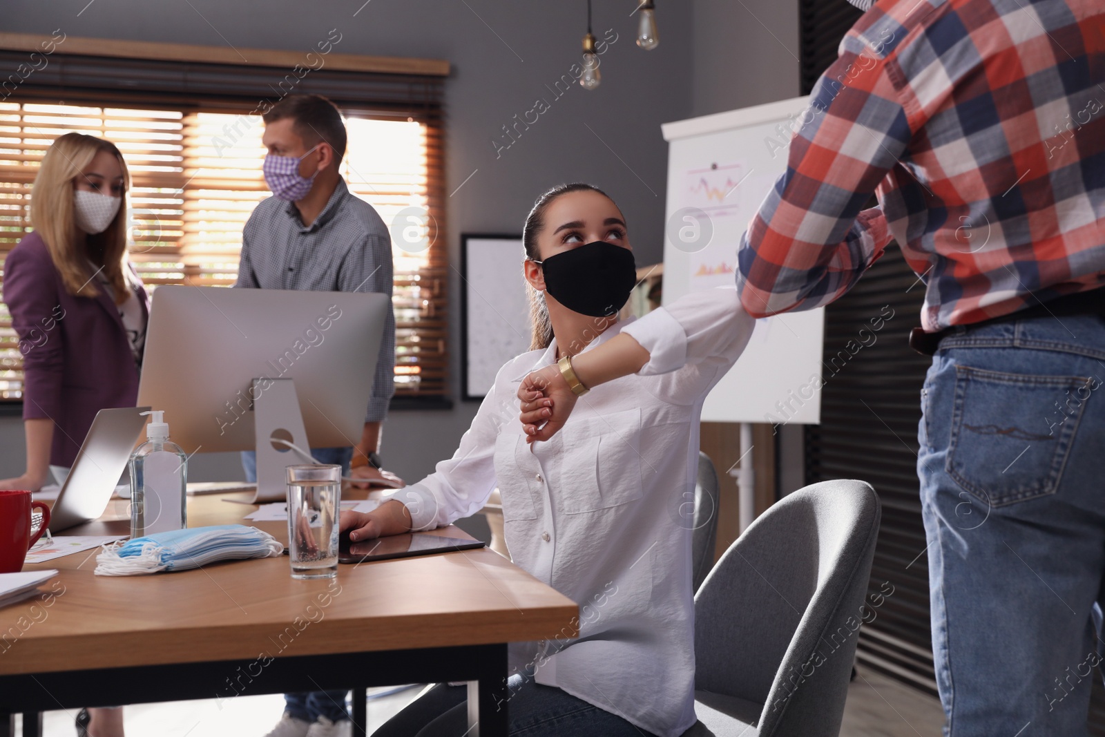 Photo of Coworkers making elbow bump in office. Informal greeting during COVID-19 pandemic