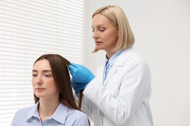 Trichologist in gloves examining patient`s hair in clinic