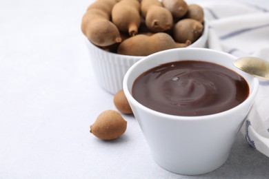 Photo of Bowl of tamarind sauce and fresh pods on light table, closeup. Space for text