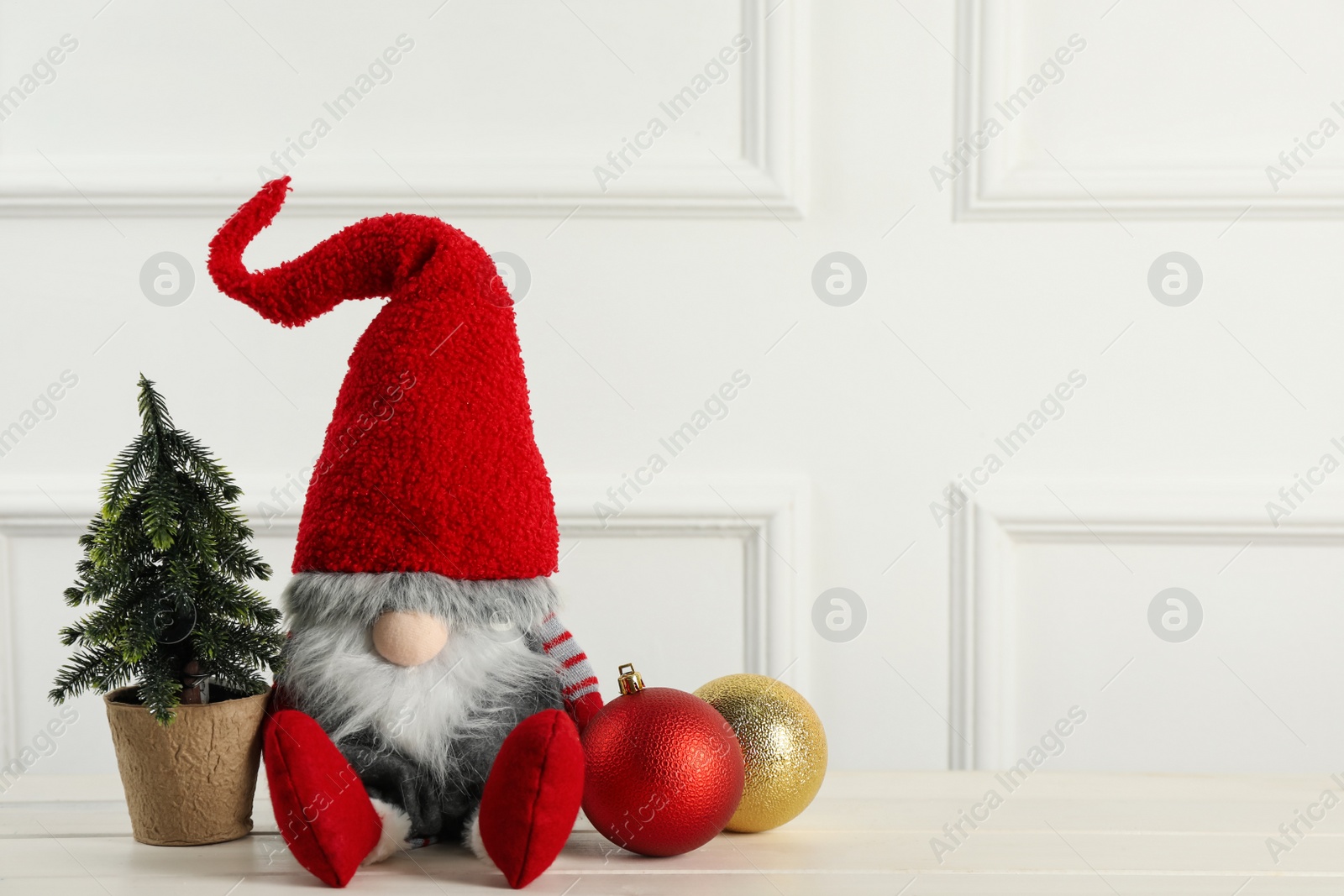 Photo of Cute Christmas gnome, small decorative fir tree and festive balls on white wooden table. Space for text