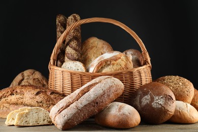 Wicker basket with different types of fresh bread on wooden table