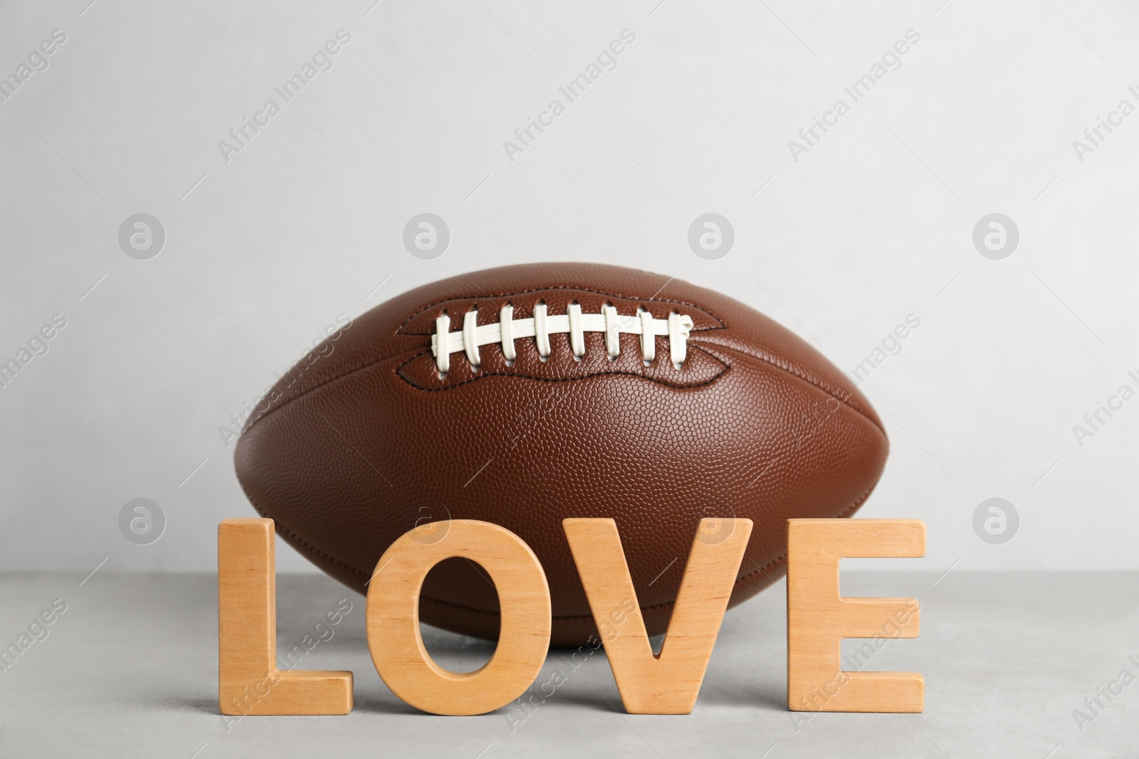 Photo of American football ball and word Love on light grey table against white background
