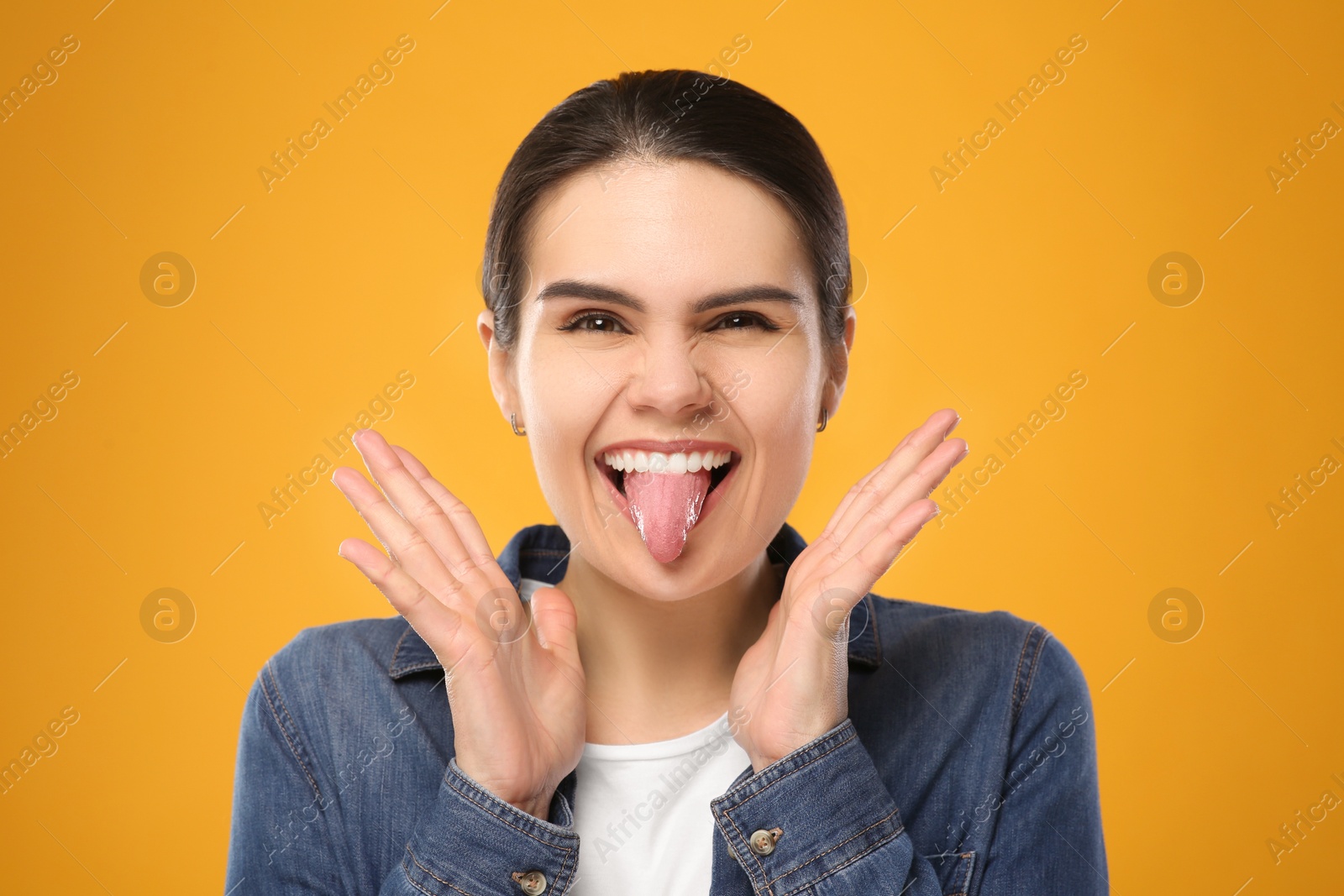 Photo of Happy young woman showing her tongue on yellow background