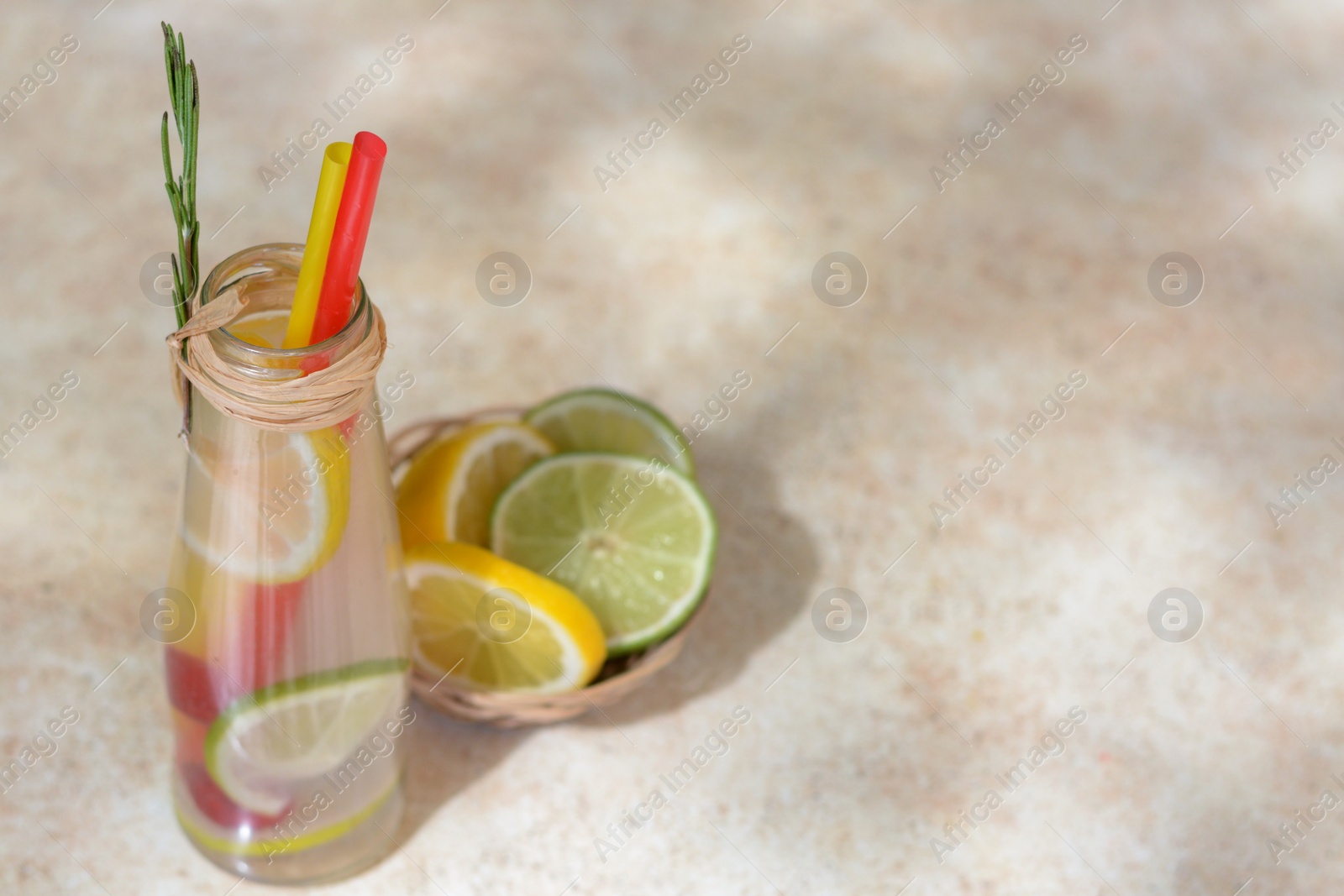 Photo of Refreshing tasty lemonade served in glass bottle and citrus fruits on beige table. Space for text