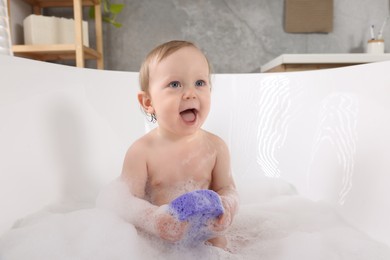 Cute little baby with sponge bathing in tub at home