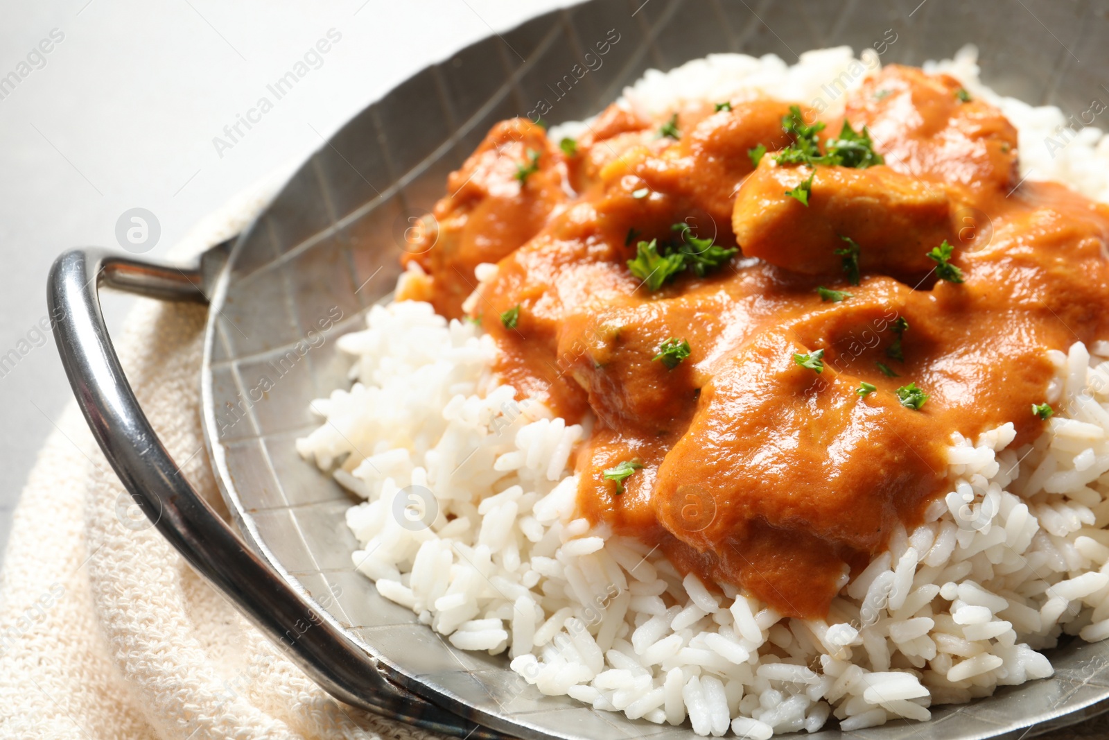 Photo of Delicious butter chicken with rice in dish and napkin on table