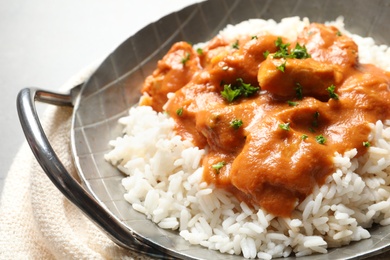 Photo of Delicious butter chicken with rice in dish and napkin on table