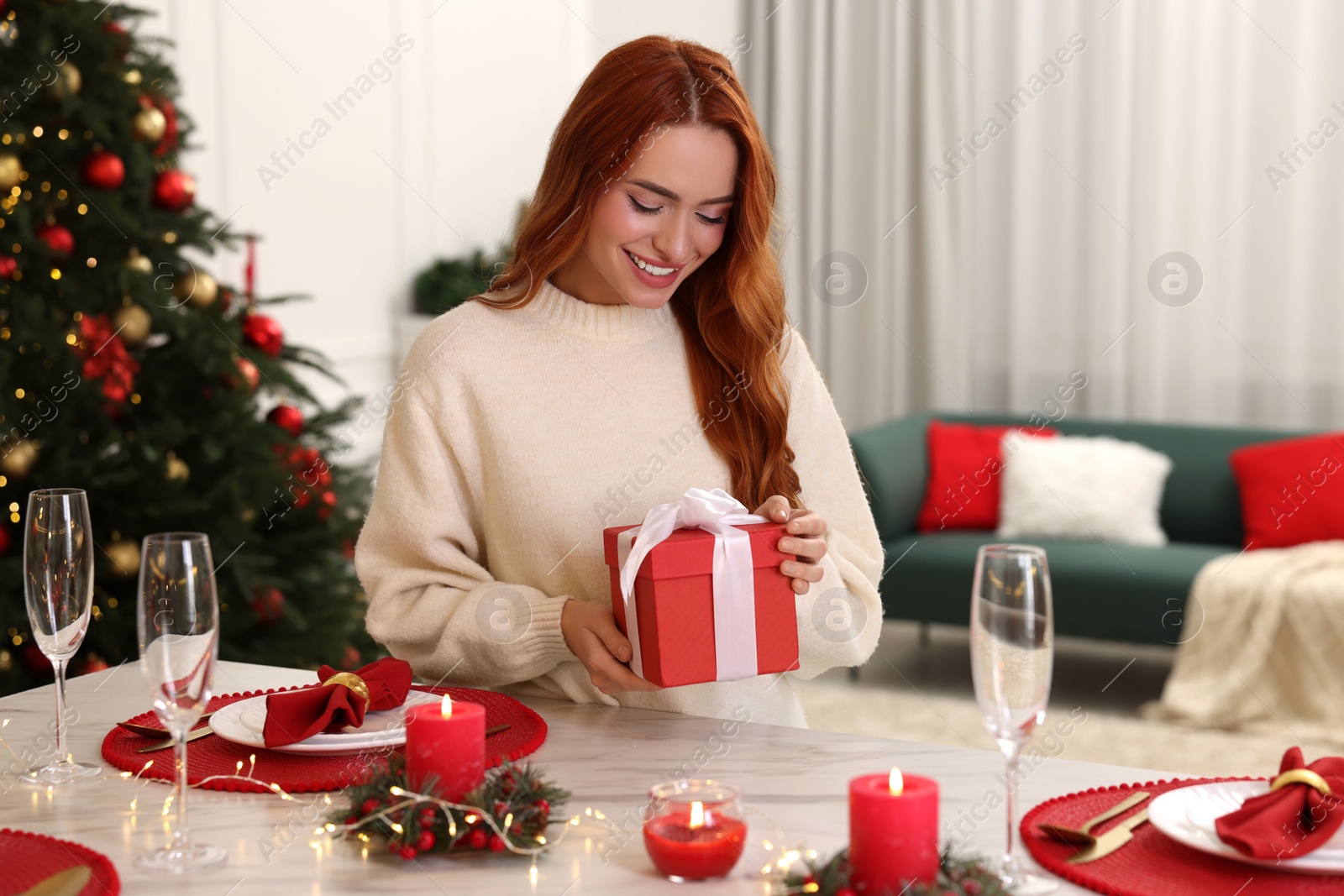 Photo of Beautiful young woman with Christmas gift at served table in room