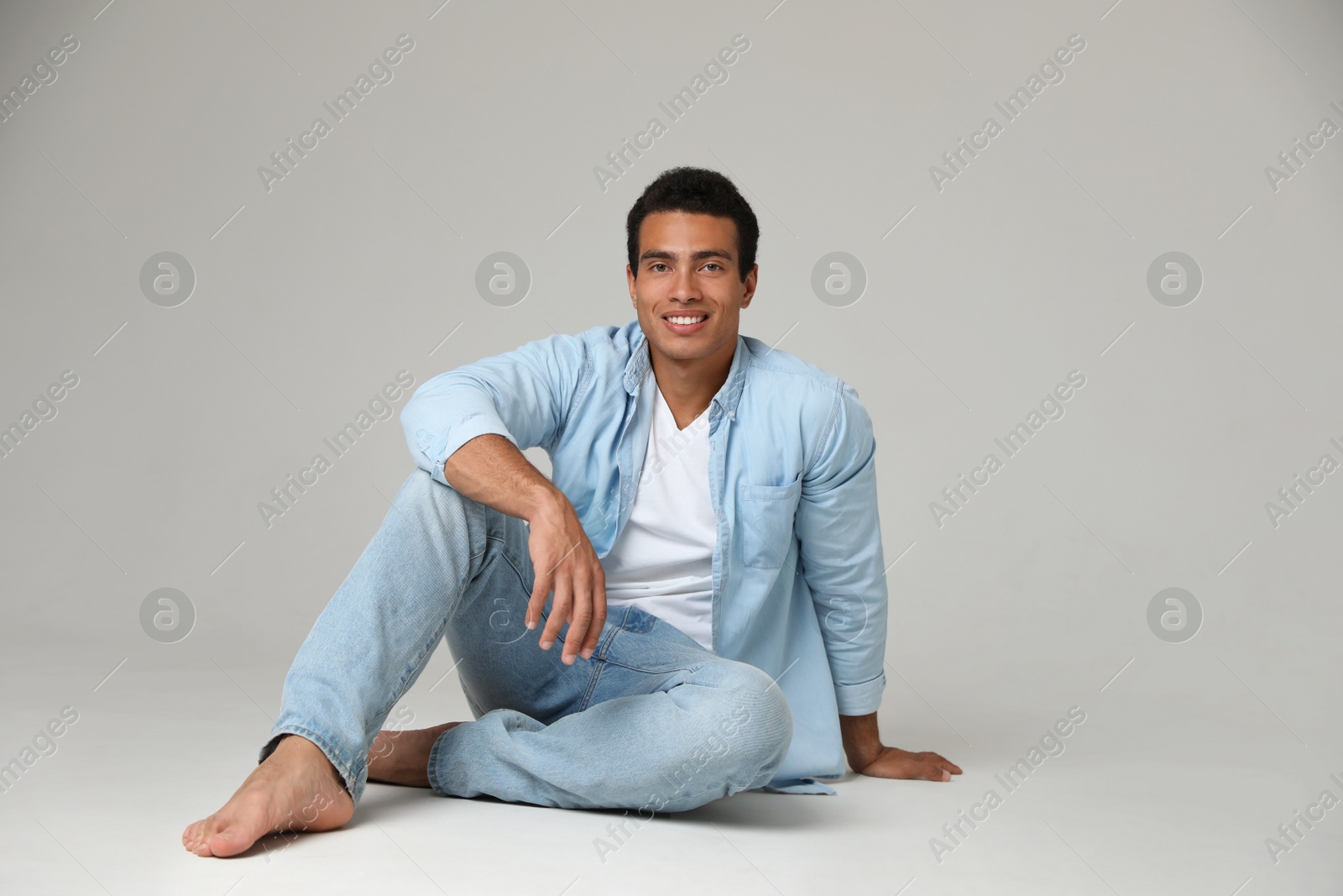 Photo of Handsome young African-American man sitting on light background. Space for text