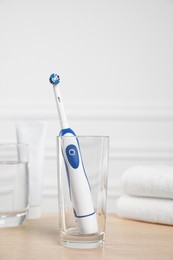 Photo of Electric toothbrush, glass of water and toiletries on wooden table