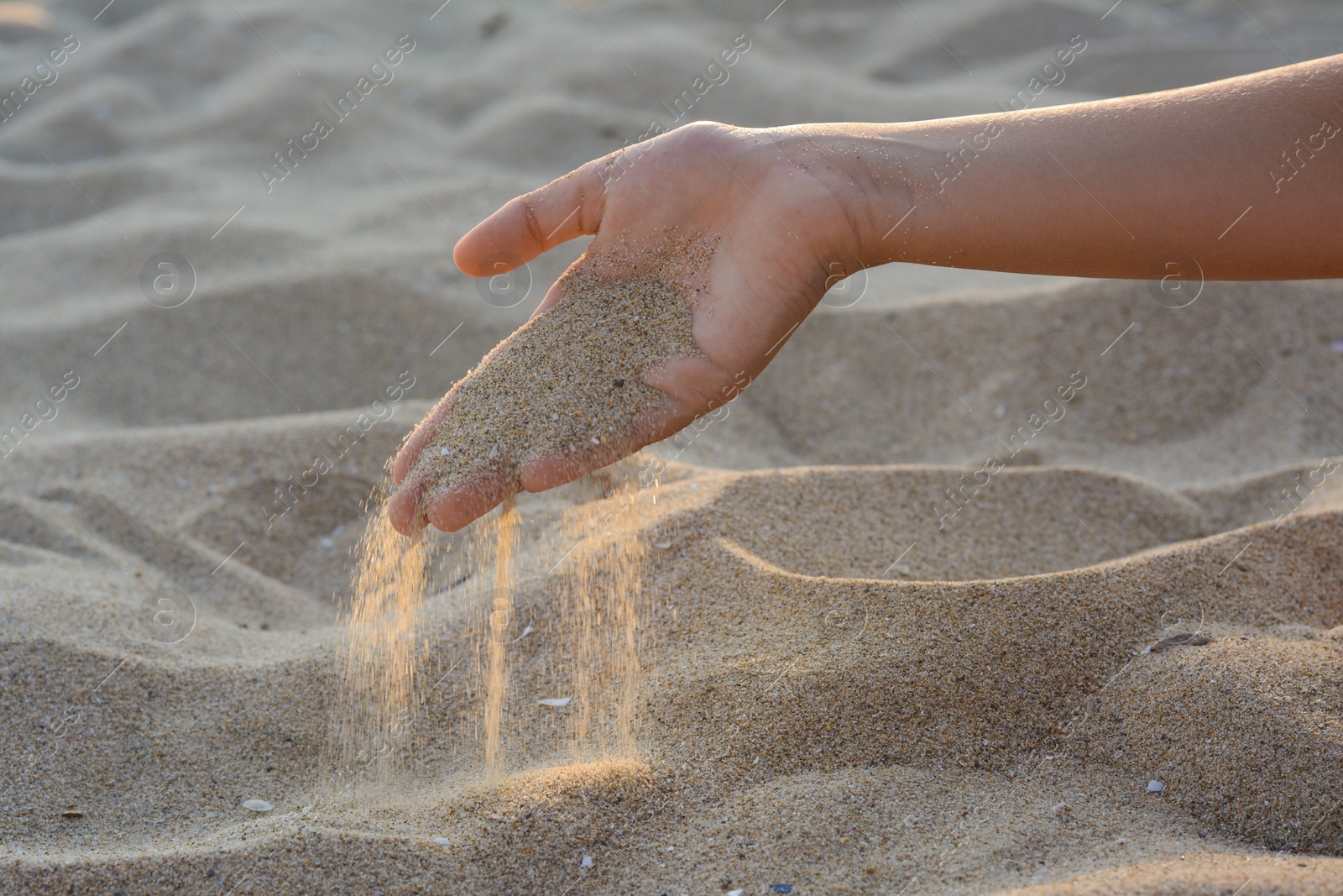 Photo of Girl pouring sand from hand outdoors, closeup. Fleeting time concept